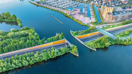 Drone view of city with road across canal, creating unique underwater bridge. Interesting houses and sailing port on water. Veluwemeer-Garderwijk Aqueduct, Netherlands.の写真素材