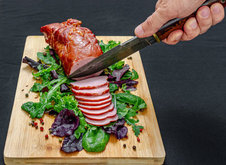 Meat baked in oven with spices on wooden board with greens. Male hands of chef or technologist cut...