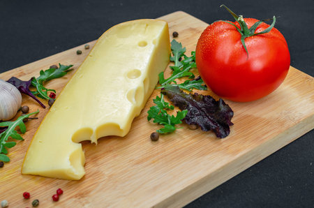 Wooden board with piece of cheese, tomato, greens. Piece of fresh cheese on wooden cutting board, served with greens and tomato. Restaurant menu.の写真素材