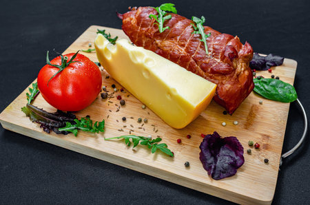 Meat, cheese, vegetables. Restaurant board with cheese, roasted pork, tomatoes and peppers, served with salad and greens. Healthy protein menu. Black background.の写真素材
