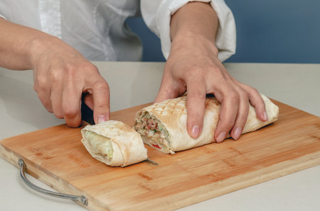 Cutting appetizing shawarma kebab into pieces with knife on wooden surface. Knife in female hands...