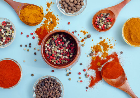 Aromatic spices and seasonings. Bright colors of Indian spices. Colored peppers in bowl on light blue background. Texture of food seasonings close-up. Vibe of spices in cooking.の写真素材