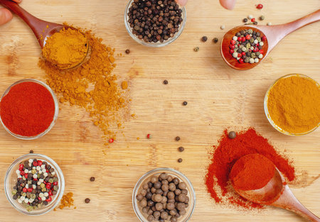 Aromatic assorted spices in wooden spoons and transparent bowls on wooden background. Perfect for...