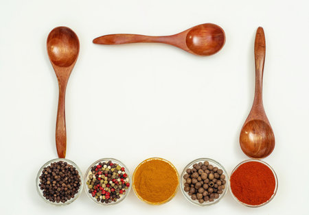 Interesting assortment with various aromatic spices and seasonings in transparent small bowls and wooden spoons on white background. Copy space.の写真素材