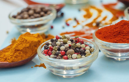 Aromatic spices and seasonings. Bright colors of Indian spices. Colored peppers in bowl on light blue background. Texture of food seasonings close-up. Vibe of spices in cooking.の写真素材