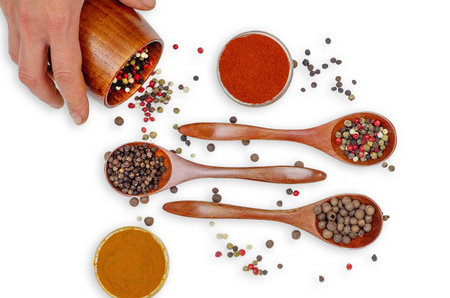 Female hand pours colored pepper from wooden mug into seasoning composition on white table. Food and cooking. Healthy eating and organic products. Culinary mood.の写真素材