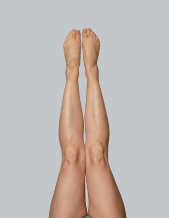 Slender bare female legs raised up. Female legs on gray background, isolated. Women's health, care and fitness exercise concept.の写真素材