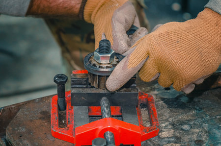 Male hands in gloves fix part for welding. Welding vice. Close-up of red table-top vice with screw handle and cast iron frame in mechanical workshop.の写真素材
