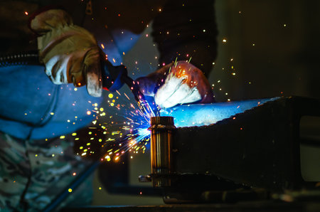 Metal welder works welding steel parts at factory in protective gloves. Production of metal...