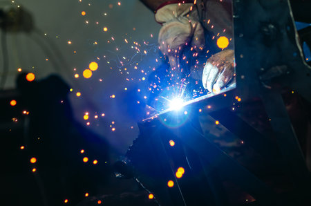 Metal welder works welding steel parts at factory in protective gloves. Production of metal...