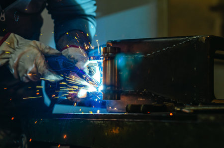 Metal welder works welding steel parts at factory in protective gloves. Production of metal...