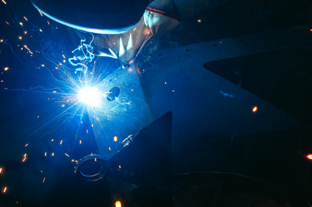 Blue light of welding work with bright sparks. Industrial welding process, welding shop worker at workplace on dark background. Metal welding factory.の写真素材