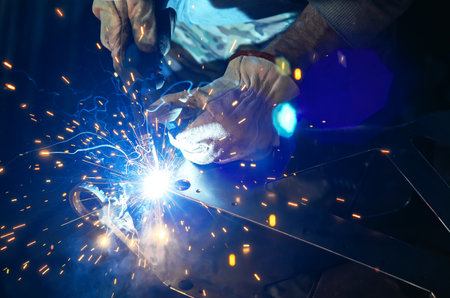 Blue light of welding work with bright sparks. Industrial welding process, welding shop worker in...