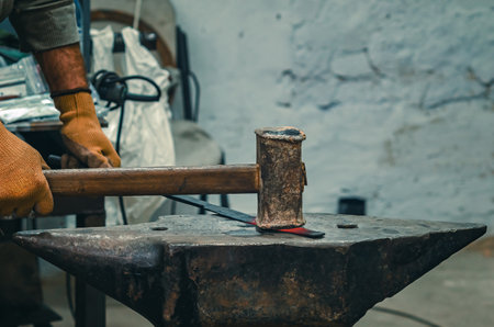 Hands of craftsman in gloves with iron hammer align iron part on stone. Vintage construction tool. Preparation for welding work.の写真素材