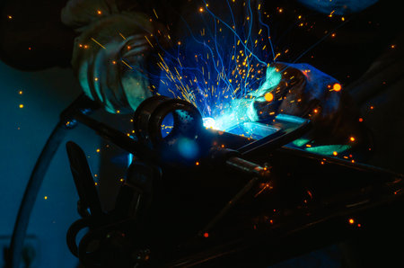 Blue light of welding work with bright sparks. Industrial welding process, welding shop worker at...
