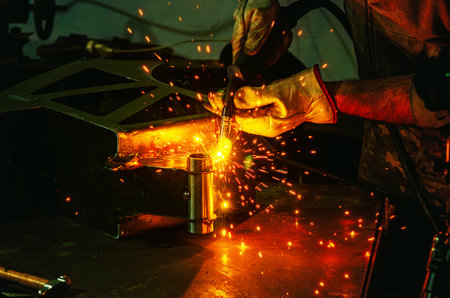 Yellow welding sparks fly around as worker welds metal part to structure in protective gloves....
