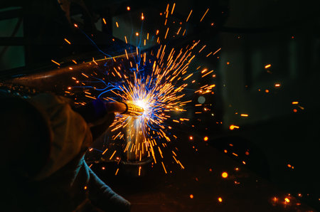 Yellow welding sparks fly around as worker welds metal part to structure in protective gloves....