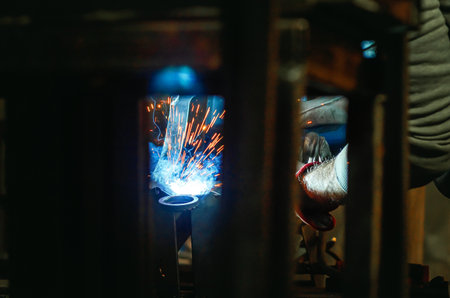 View through metal parts covering welding machine. Yellow sparks and blue smoke fly from welding...