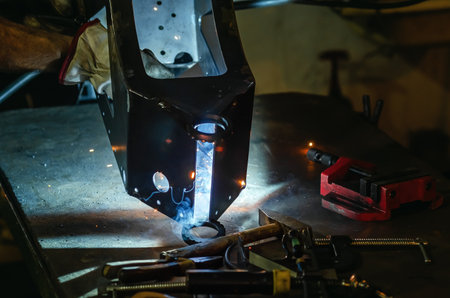 View through metal parts covering device, master welds parts. Yellow sparks and blue smoke fly from...