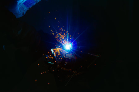 Blue light of welding work with bright sparks. Industrial welding process, welding shop worker at workplace on dark background. Metal welding factory.の写真素材