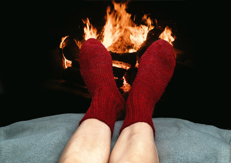 Minimalistic winter-themed image showing relaxed legs in bright red knitted socks near burning fireplace, ideal for concepts of warmth, comfort, and seasonal holidays.の写真素材