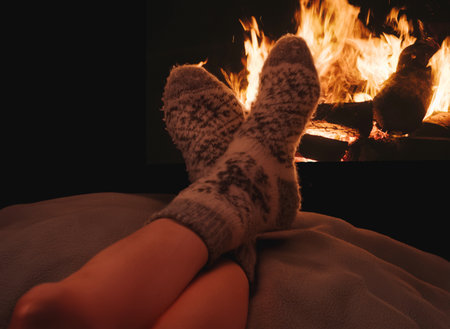 Warm winter scene with feet in gray wool socks resting by burning fireplace. Feeling of relaxation, comfort and cozy holiday evenings at home.の写真素材
