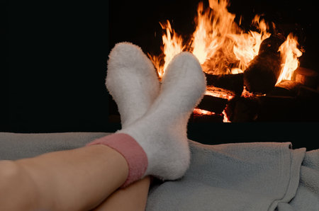 Minimalist winter image showing relaxed feet in white fluffy socks by blazing fireplace is perfect for concepts of warmth, comfort, and seasonal celebrations.の写真素材
