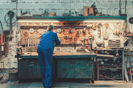 Professional worker in blue work uniform and orange protective gloves in production workshop. Image...
