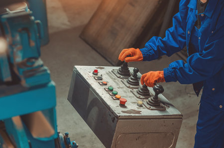 Industrial worker in blue protective uniform and orange gloves operating control panel with...