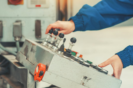 Female hands of industrial worker in blue protective uniform working with control panel with...