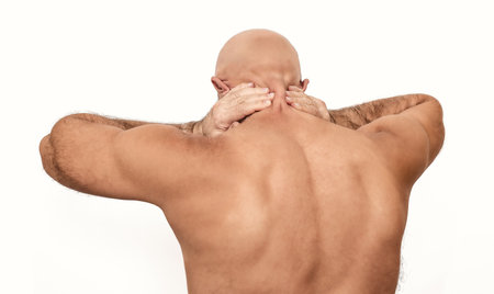 Neck pain in bald man. White background, isolated. Man suffering from neck pain, hands behind head....