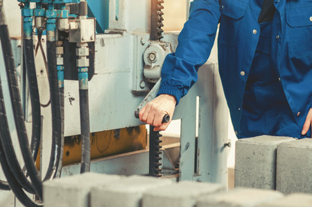 Factory technician in blue workwear adjusting industrial machine controls on production line. Modern...
