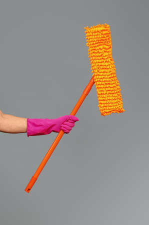 Mop for washing surfaces in hand in pink protective glove on gray background, isolated. Concept of...