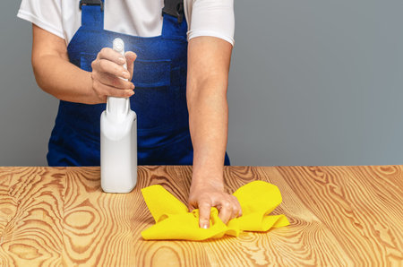 Worker in blue overalls polishes wooden furniture from dust, dirt and stains. Professional cleaning,...