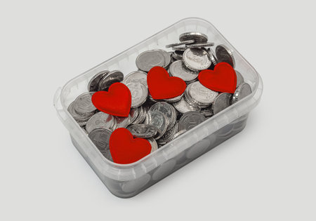 Several small red hearts placed on pile of metal coins in transparent container on neutral gray background. Concept of charity, donation, love and financial support. Top view.の写真素材