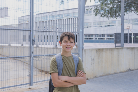 Cheerful child carrying his backpack standing in front of the school.の写真素材