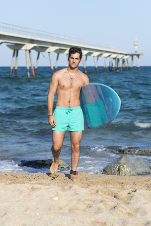 Young attractive surfer holding his surfboard at the beachの写真素材