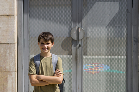 Cheerful child carrying his backpack standing in front of the school.の写真素材