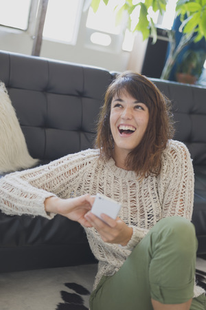 Cheerful woman speaking on mobile phone, sitting on living room floorの写真素材