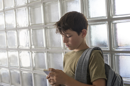 Student resting on the corridor of a school and playing with a mobile phoneの写真素材
