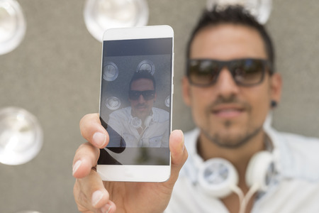 Closeup outdoors shot of young  man with headphones taking a selfie with smart phoneの写真素材