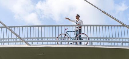 Casual wearing man looking and pointing away over a bridgeの写真素材