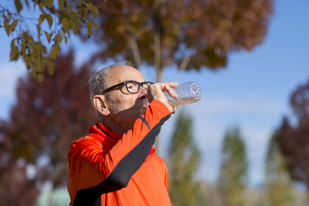 Handsome senior jogging man drinking fresh water from bottle after morning runの写真素材