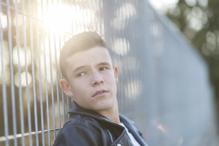 Portrait of a stylish teenager standing against a fence on a city parkの写真素材