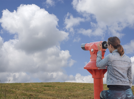 Young woman looking through tourist telescope, exploring landscape.の写真素材