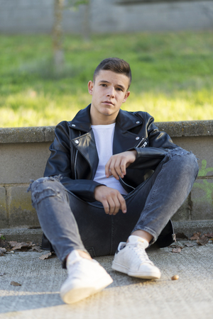 Young male sitting outdoors wearing black leather jacket.の写真素材