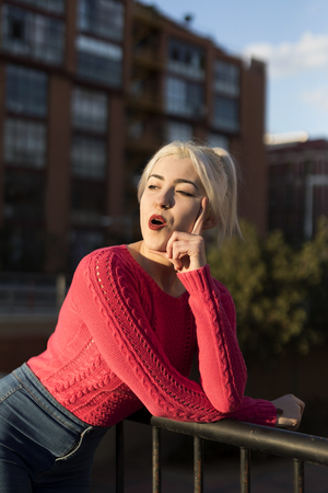 Portrait of a young blonde woman gesturing in the street wearing a red sweeterの写真素材