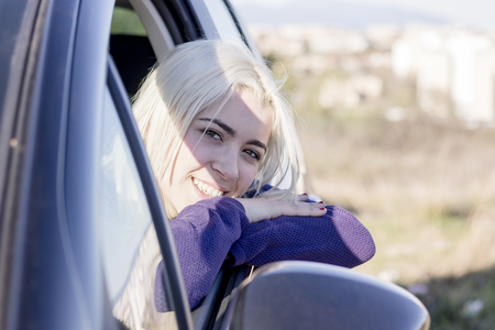 Portrait of cute, fun, young woman sitting in the car looking out the window, leaning on the arm