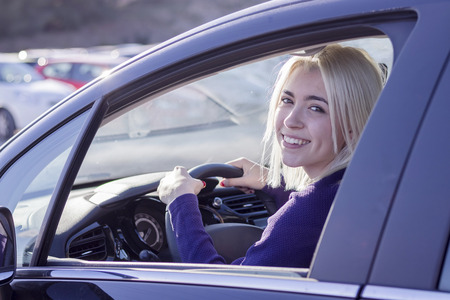 Young woman driving a car in the city. Portrait of a beautiful woman in a car, looking out of the window and smiling. Travel and vacations conceptsの写真素材