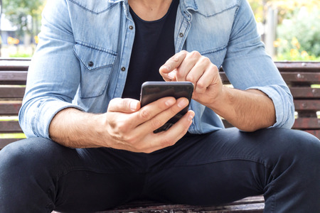 Close up shot of man hands using mobile while sitting on the bench in the city.の写真素材